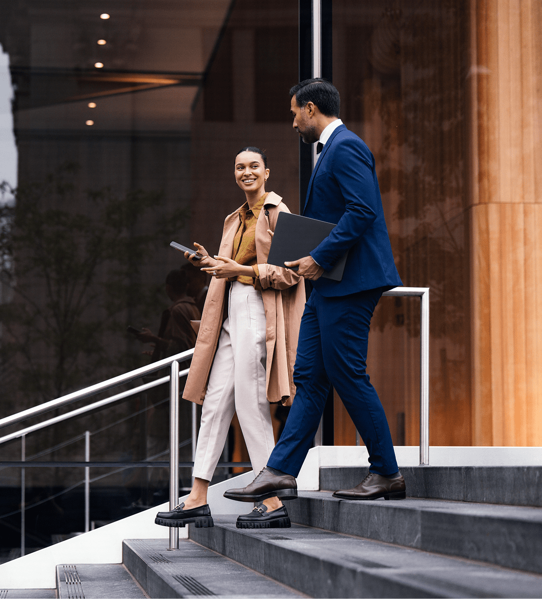 Two professionals walk down stairs outside a modern building, engaged in conversation.